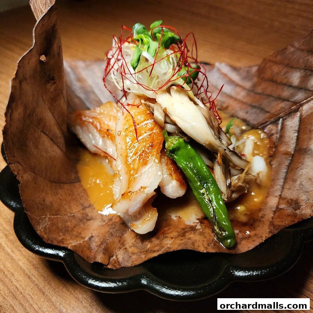A beautifully plated dish of grilled fish with mushrooms and a green pepper on a large leaf.