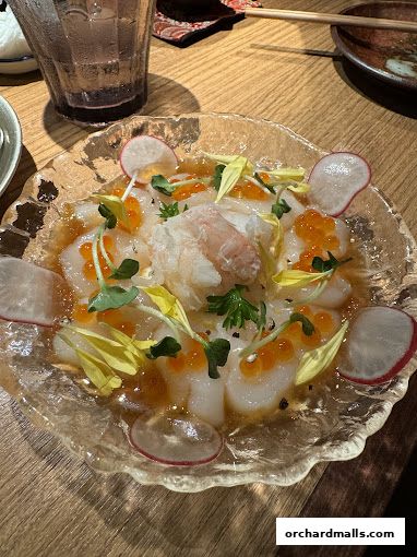 A beautifully presented scallop dish with roe, radish, and microgreens in a clear bowl.