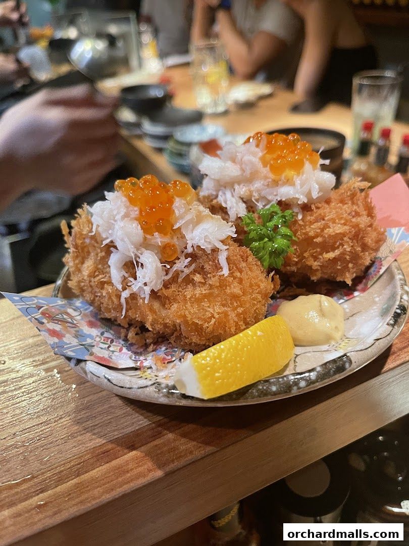 Two crispy fried seafood croquettes topped with crab meat and ikura, served with lemon and mustard.