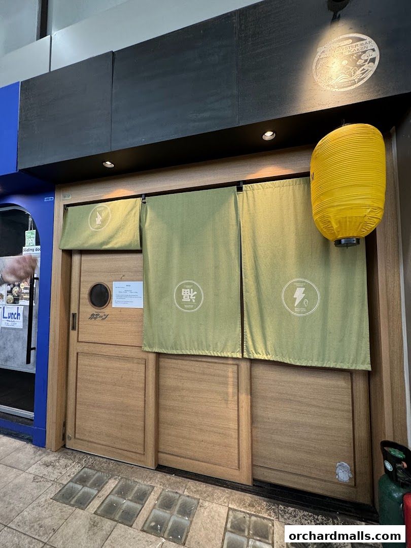 The entrance of Kakiin Oyster Bar features wooden doors, green curtains, and a yellow lantern.