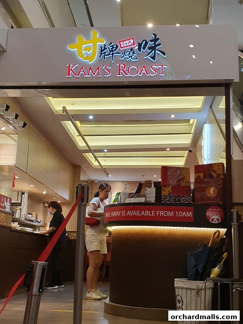 The entrance of Kam's Roast Express, a shop specializing in roasted meats, with customers and staff visible.