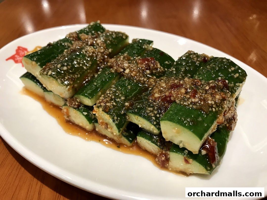 A plate of sliced cucumbers topped with a savory sauce and sesame seeds.