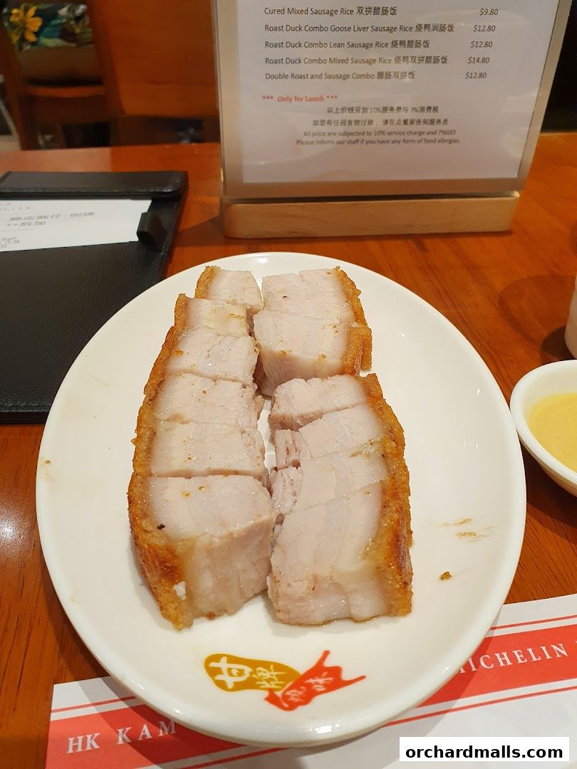 A plate of crispy roast pork sits on a table next to a menu at Kams Roast Express.