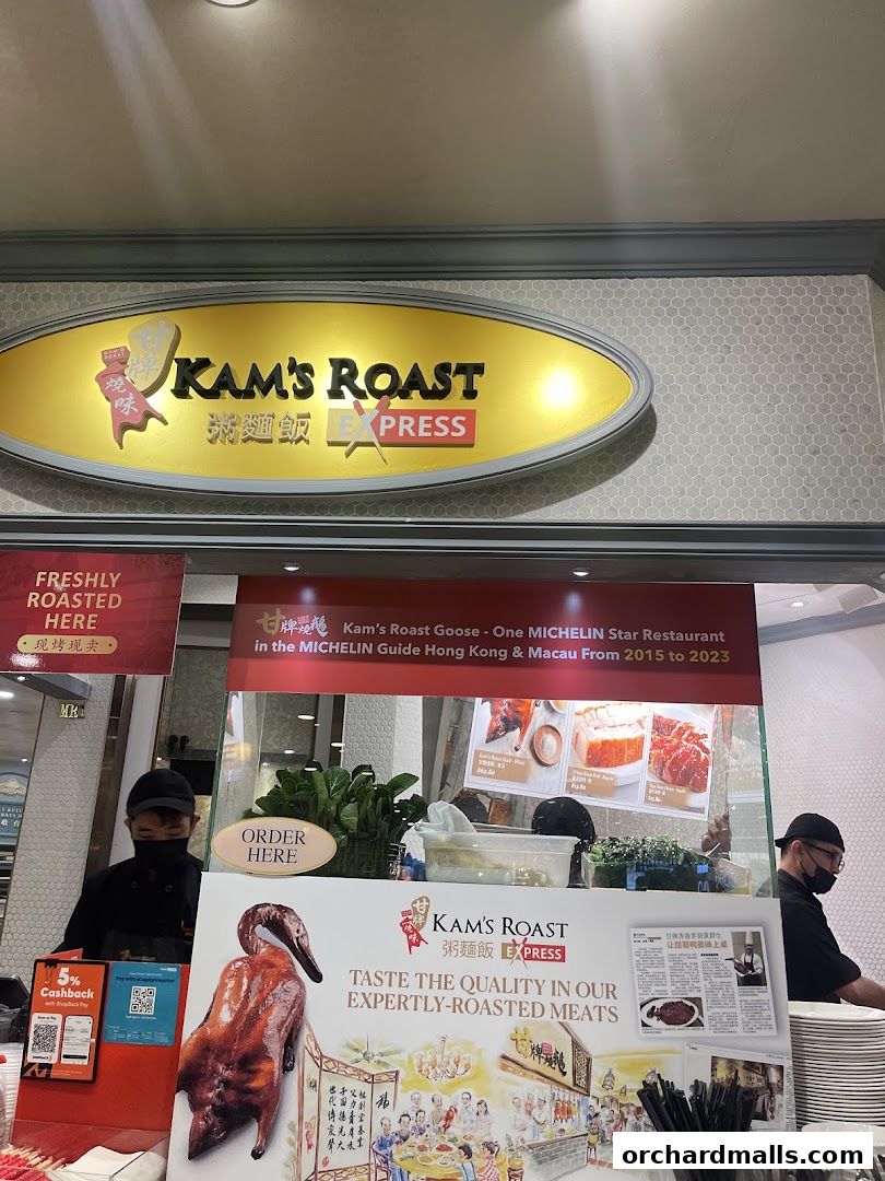 The entrance of Kam's Roast Express, featuring its prominent signage and a display of roasted meats.