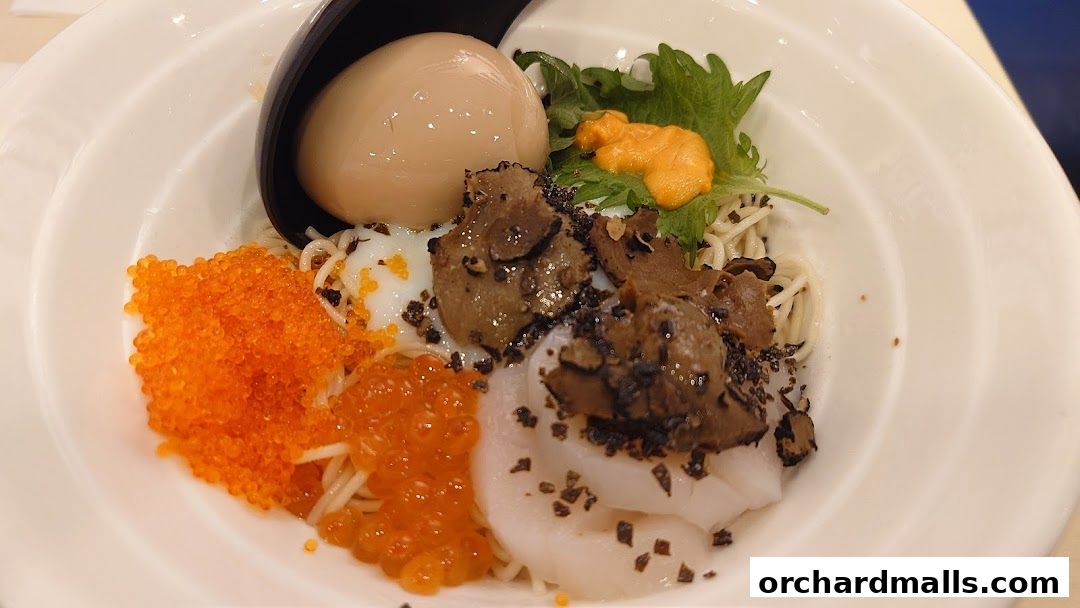 A close-up of a gourmet ramen dish with various toppings including egg, roe, uni, and truffle.