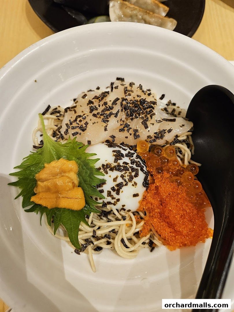 A bowl of ramen with uni, ikura, scallops, and a soft-boiled egg, topped with seaweed.