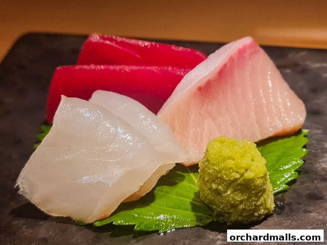 Close-up of fresh sashimi with tuna, white fish, and wasabi on a dark plate.