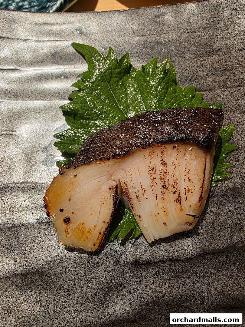 A perfectly grilled fish fillet served on a bed of fresh green leaves.