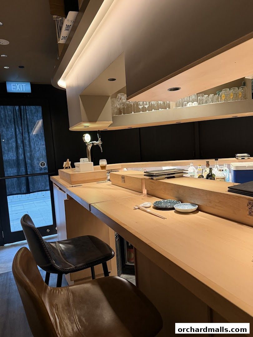 Interior of a sushi bar with a wooden counter, chairs, and bar stools.