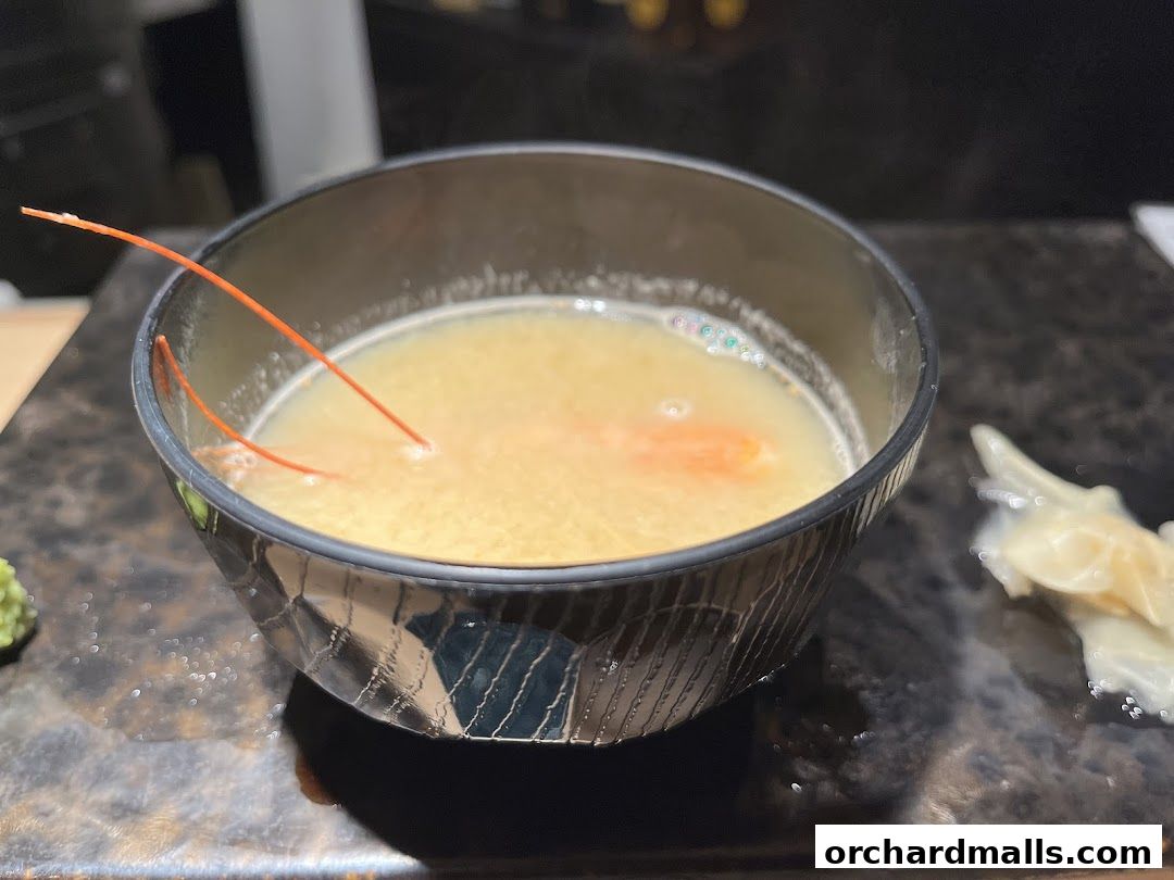 A close-up of a steaming bowl of Japanese soup with a piece of seafood and garnish.
