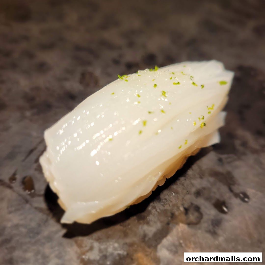 A close-up of a single piece of sushi with white fish and green zest.