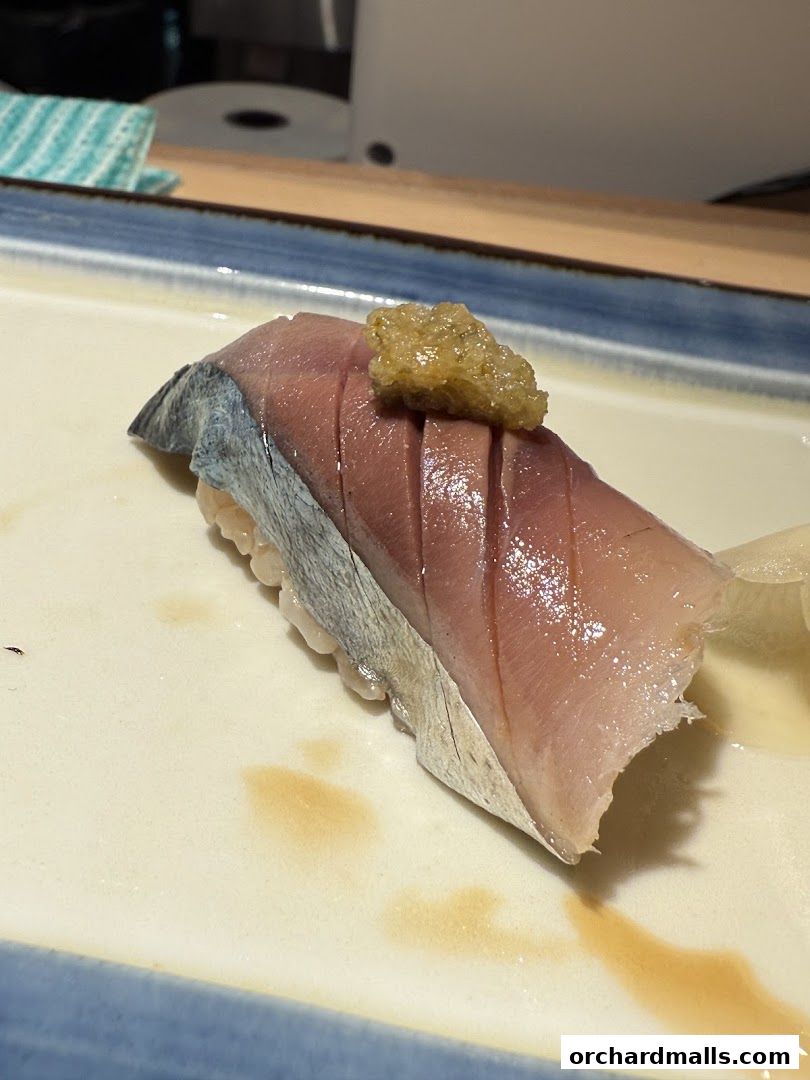 A close-up of a single piece of sushi with fish and a topping on a plate.