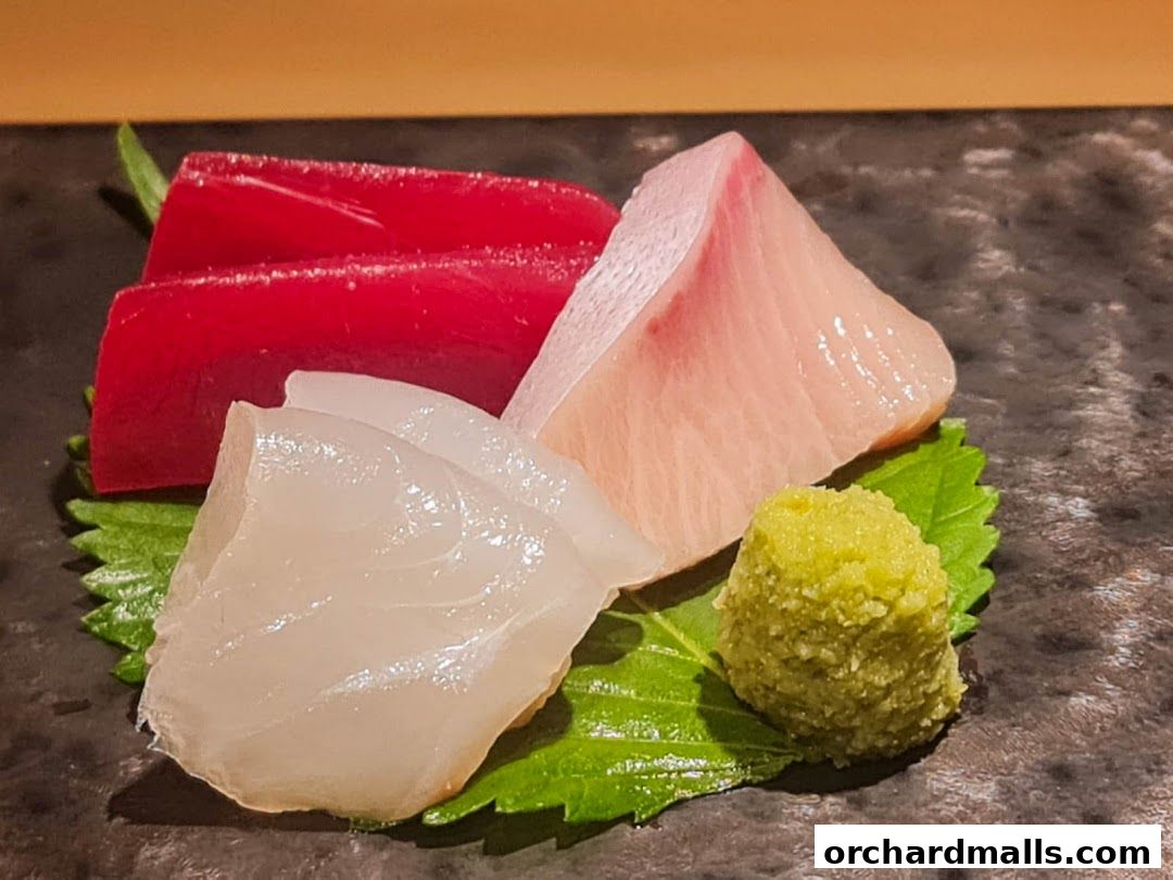 A close-up of fresh sashimi with wasabi and garnishes on a dark plate.
