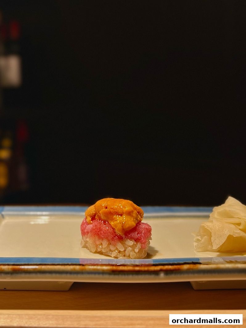 A single piece of sushi with tuna and sea urchin on a plate with ginger.
