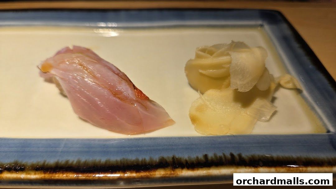 A close-up of a piece of sushi with pickled ginger on a blue-rimmed plate.