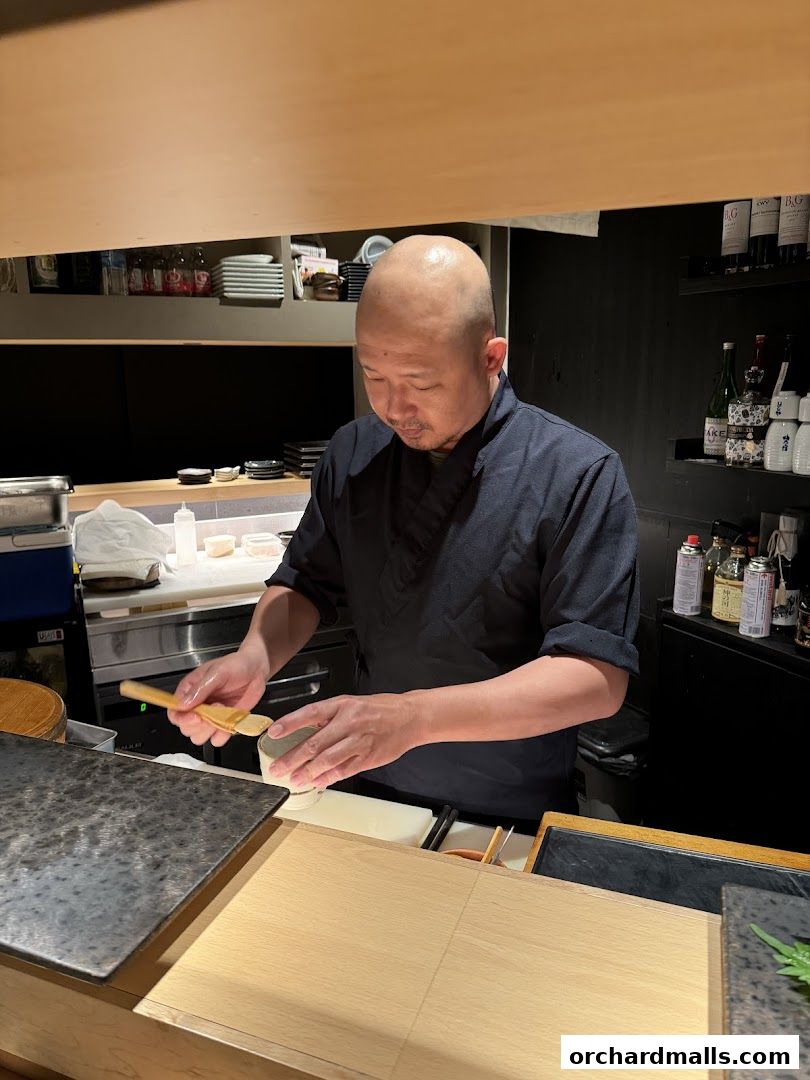 A sushi chef prepares ingredients behind a counter in a Japanese restaurant.