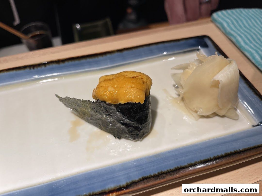 A close-up of a uni sushi roll with pickled ginger on a white plate.
