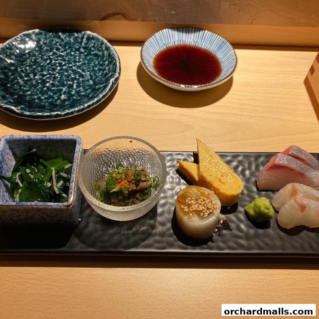 A beautifully presented Japanese appetizer platter with sashimi, tamagoyaki, and greens.