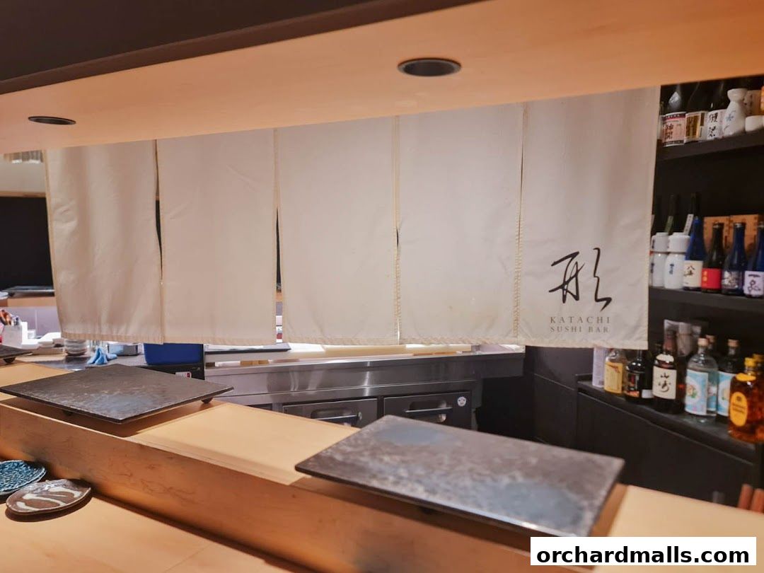 Interior of a sushi bar with a noren curtain and bottles of sake on shelves.