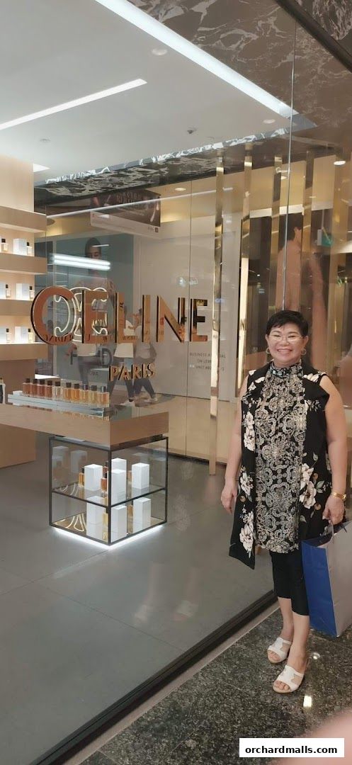 A woman stands in front of a Celine Paris store displaying perfumes and skincare products.