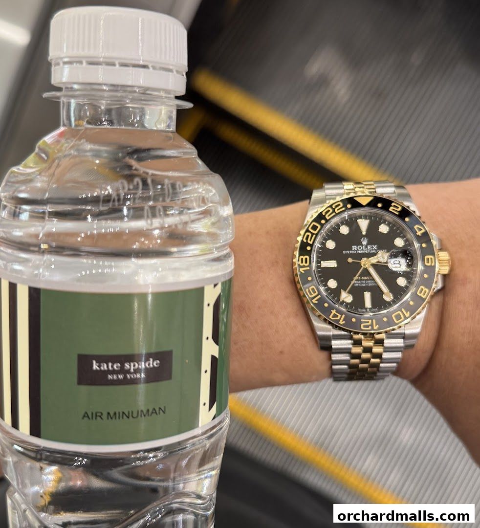 A bottle of Kate Spade water next to a Rolex watch on a wrist.