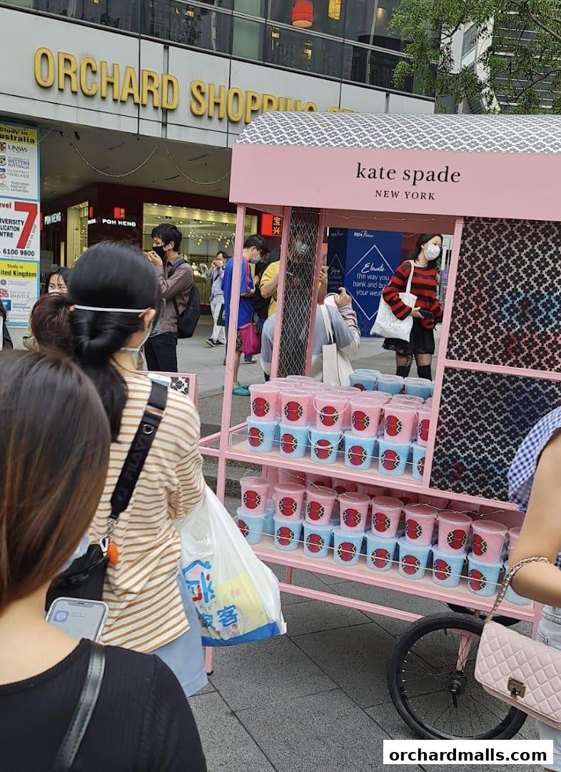 A pink Kate Spade New York cart displays rows of pink and blue buckets with a red logo.