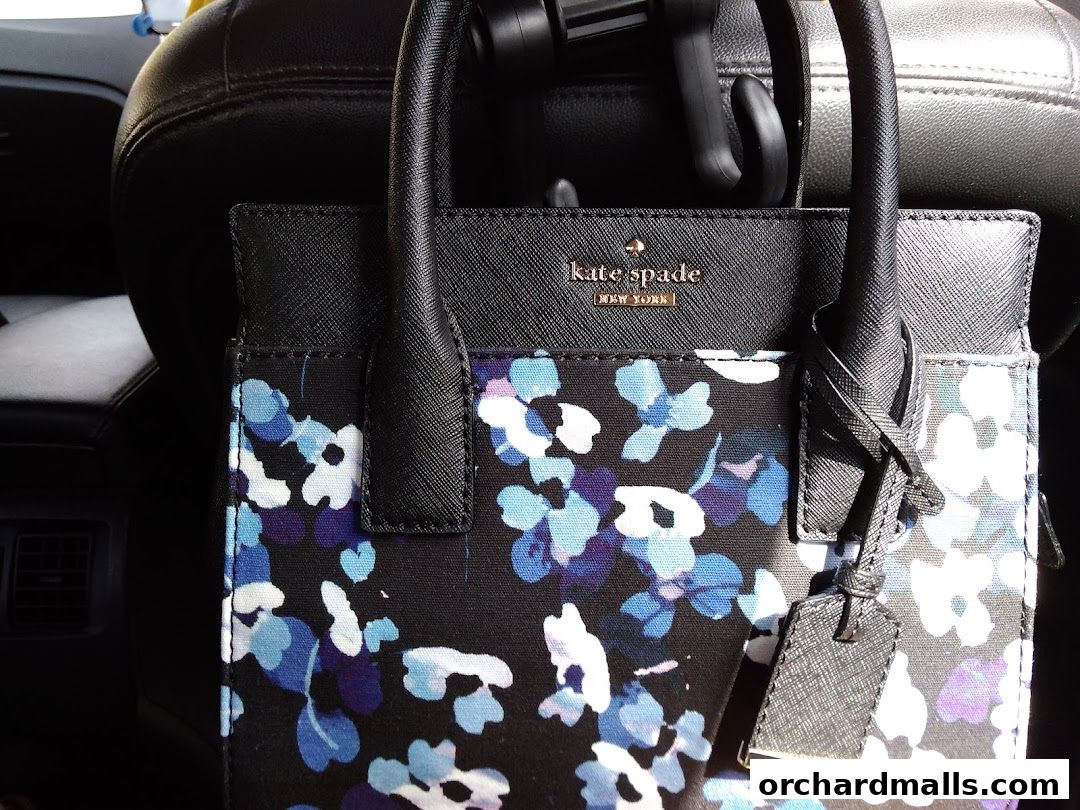 A Kate Spade New York handbag with a floral print sits on a car seat.