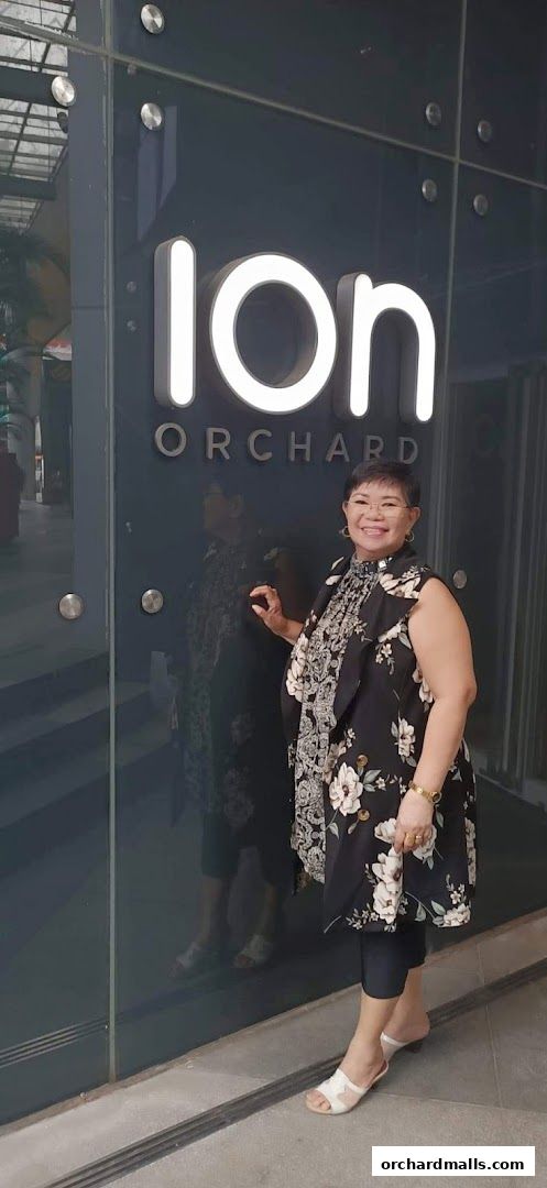 A woman poses in front of the illuminated 'ION ORCHARD' sign on a dark, reflective surface.