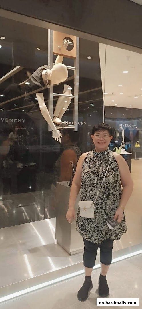 A woman poses in front of a Givenchy store window display with mannequins.