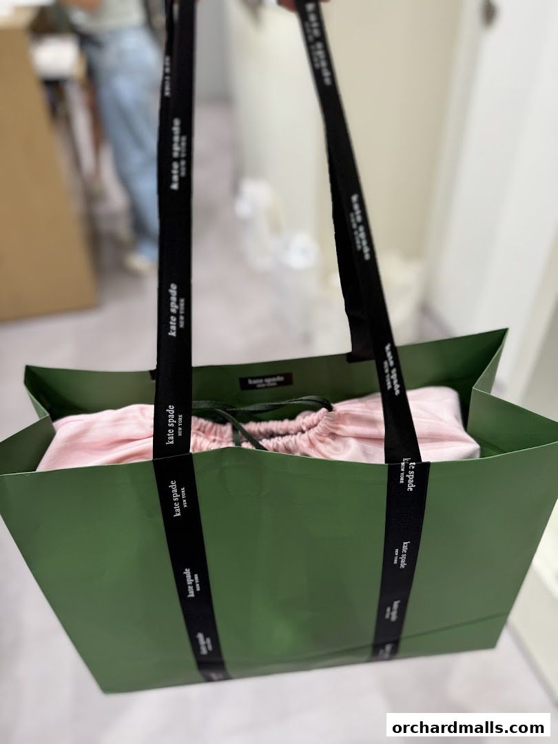 A green Kate Spade shopping bag with pink clothing and branded ribbon handles.