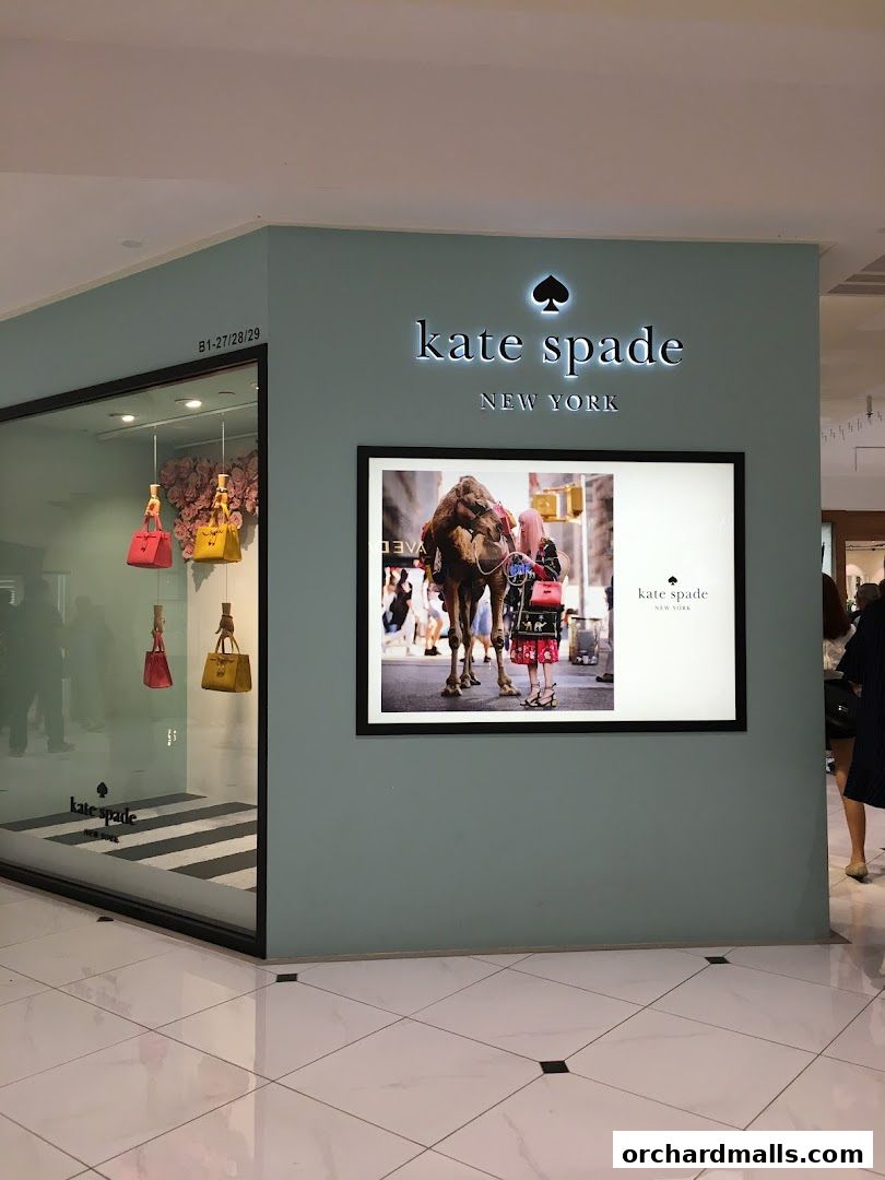 Kate Spade New York store entrance with handbags displayed in the window and a large advertisement.