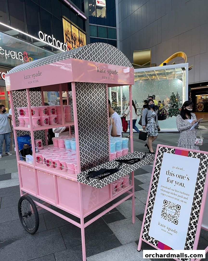 A pink Kate Spade New York cart offering sweet treats and a QR code for a sticker pack.