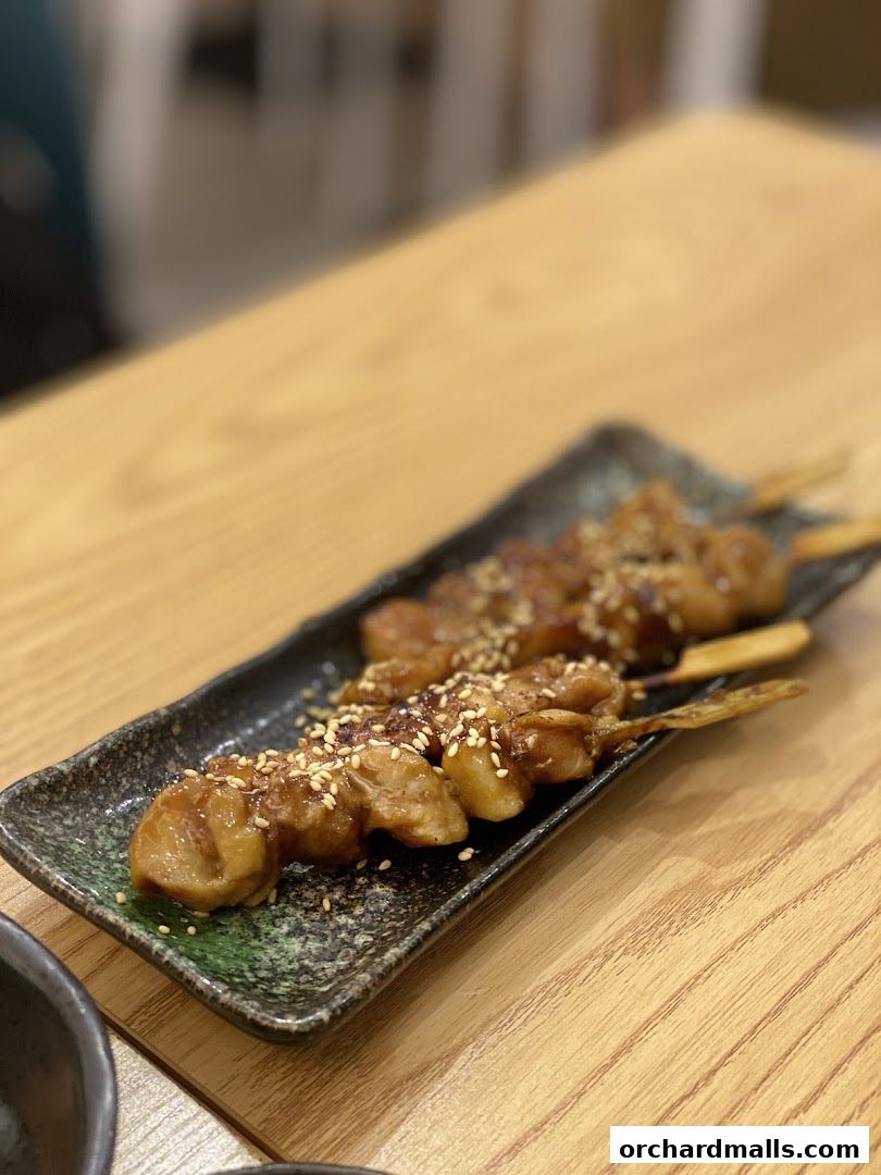 A close-up of grilled chicken skewers with sesame seeds on a dark plate.
