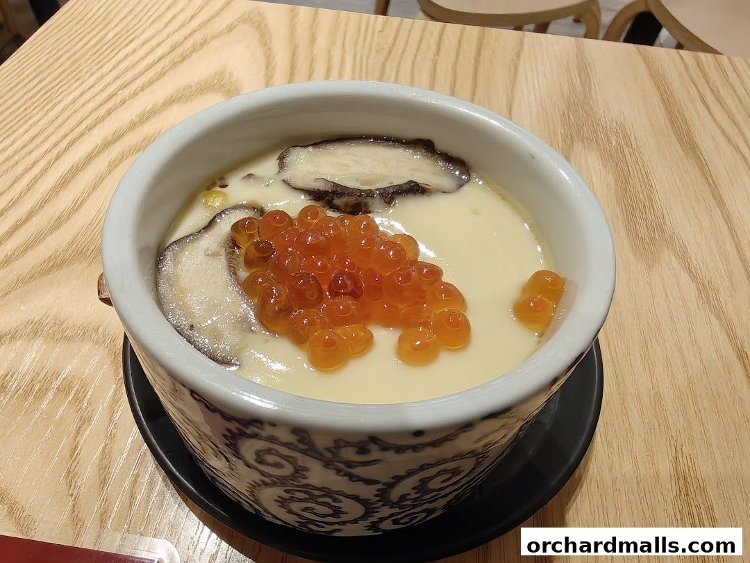 A close-up of a Japanese steamed egg custard dish with salmon roe and mushrooms.