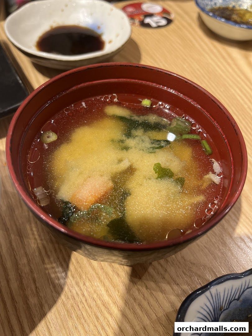 A close-up of a steaming bowl of miso soup with tofu, seaweed, and green onions.