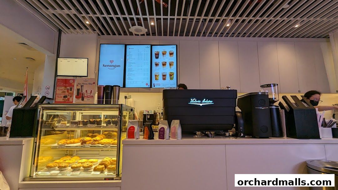 Kenangan Coffee shop counter with pastries, coffee machine, and digital menu displays.