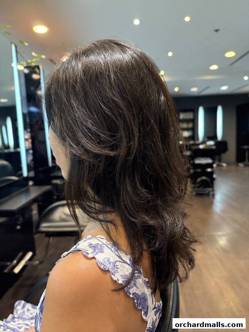 A woman with dark, layered hair sits in a salon chair, showcasing a fresh haircut.