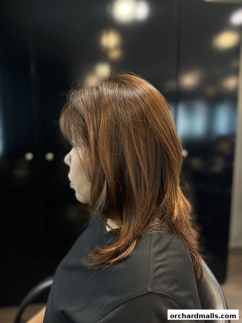 A woman with stylish, layered brown hair is shown from the side in a salon.