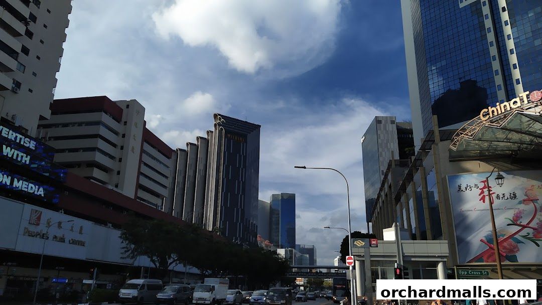 A street view of modern buildings and a busy road with vehicles under a cloudy sky.