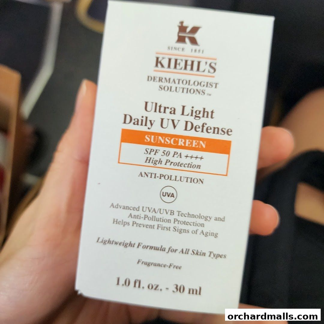 A hand holds a Kiehl's Ultra Light Daily UV Defense sunscreen box.