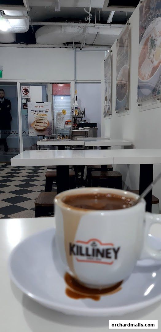 A close-up of a Killiney Kopitiam coffee cup with a blurred background of the shop interior.