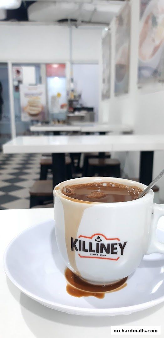 A close-up of a Killiney Kopitiam coffee cup with coffee spilled on the saucer.