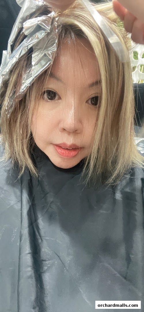 A woman with blonde hair is getting her hair colored with foils and a cape.