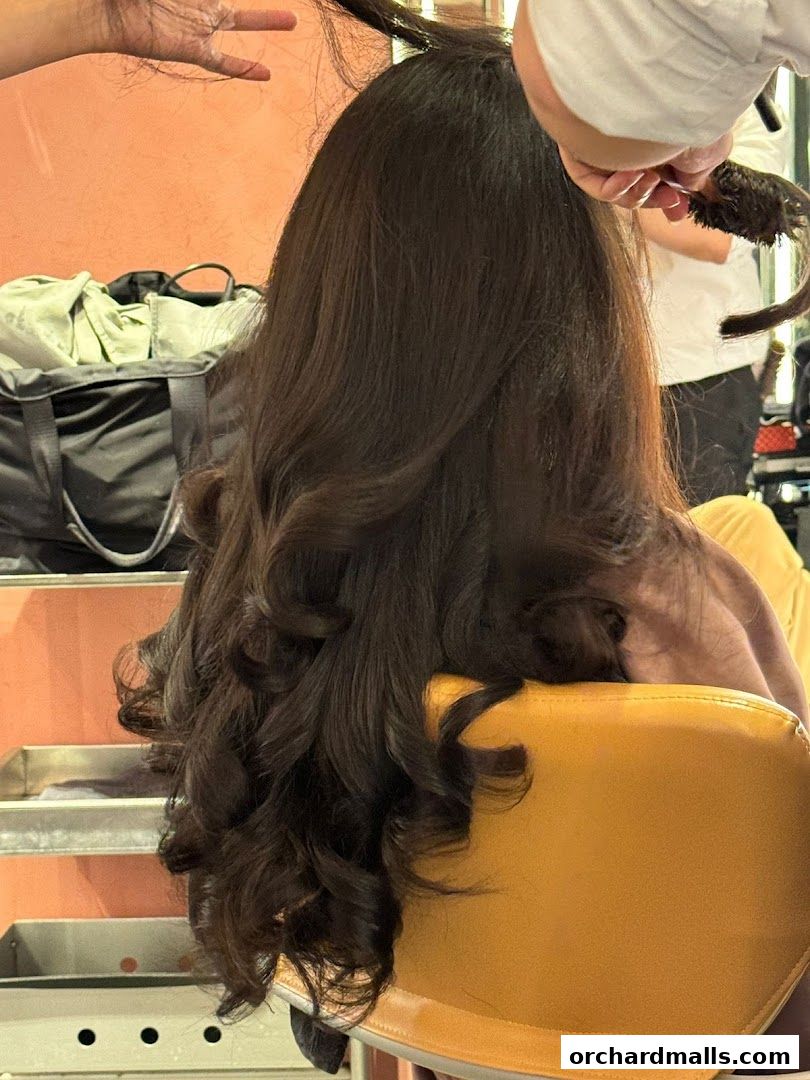 A person's long, dark hair is being styled with curls in a salon.