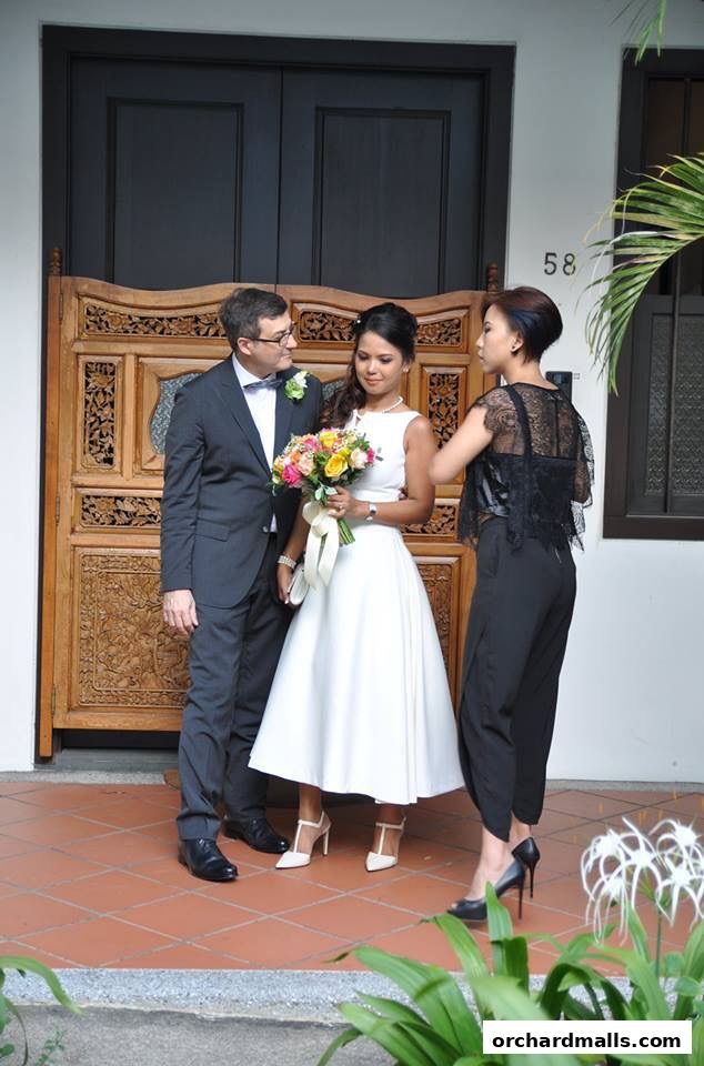 A bride, groom, and another woman stand in front of a decorative wooden door.