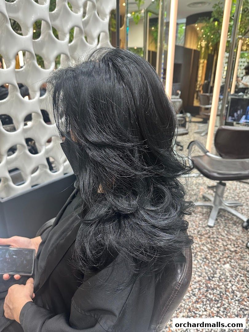 A person with voluminous black hair sits in a salon chair, holding a phone.