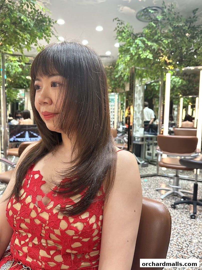 A woman with a new haircut sits in a salon chair, looking to the side.
