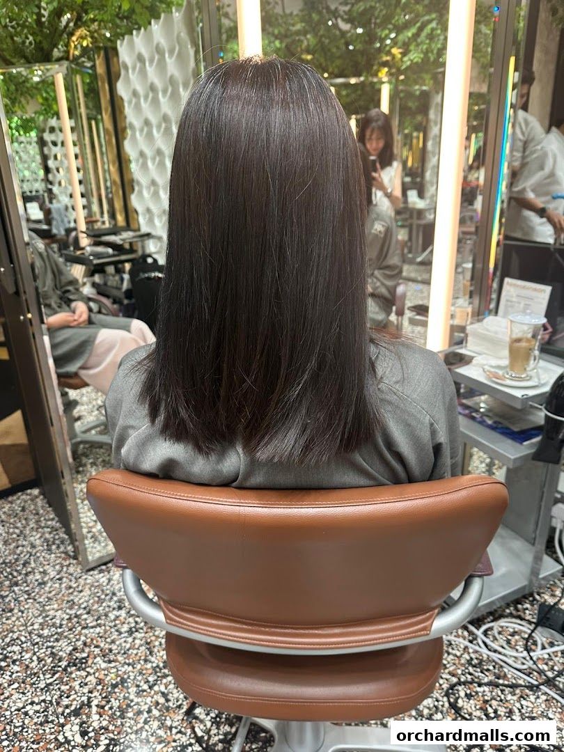 A person sits in a salon chair with long, dark hair, facing away from the camera.