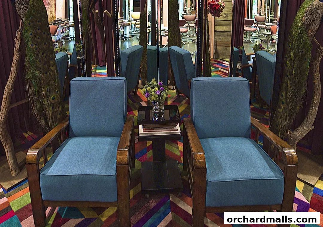 Two blue armchairs flank a small table with books and flowers, in a salon with mirrors and peacock feathers.