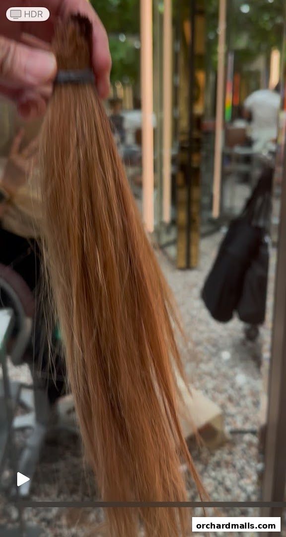 A hand holds a bundle of reddish-brown hair tied with a black band.